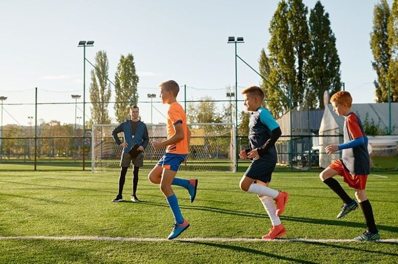 Unga fotbollsspelare joggar under en uppvärmning på konstgräs